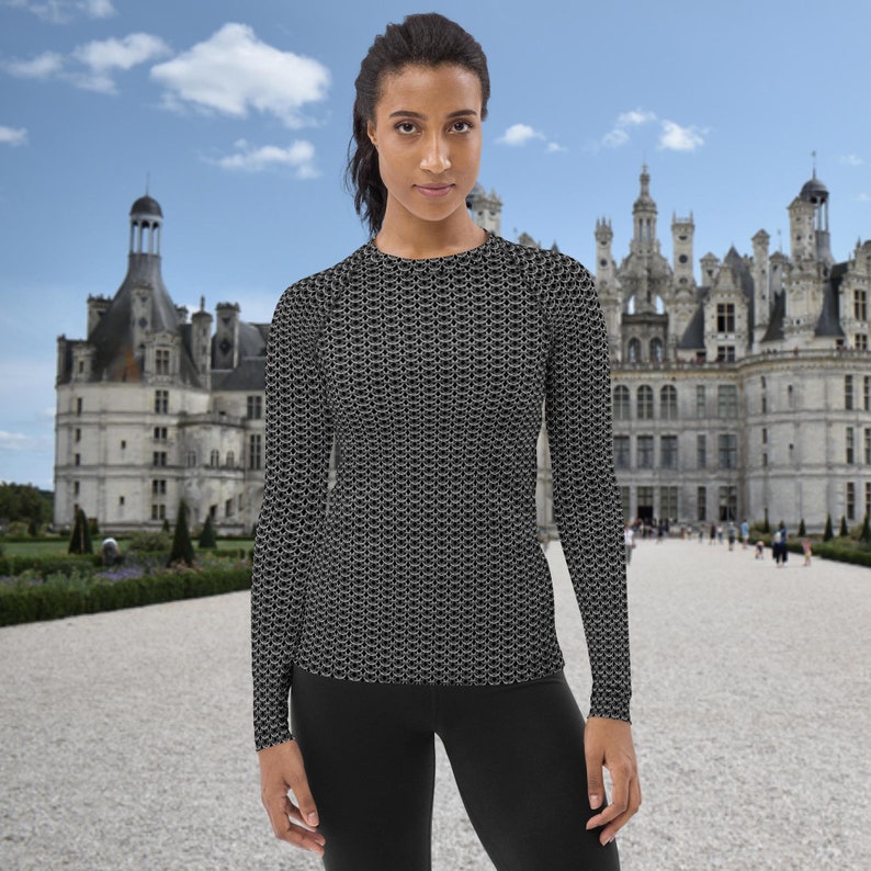 May include: A black long-sleeved shirt with a chainmail pattern. The shirt is being worn by a person standing in front of a large white castle.