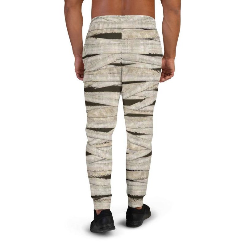 May include: A pair of sweatpants with a mummy-inspired print. The sweatpants are beige with brown bandages wrapping around the legs.
