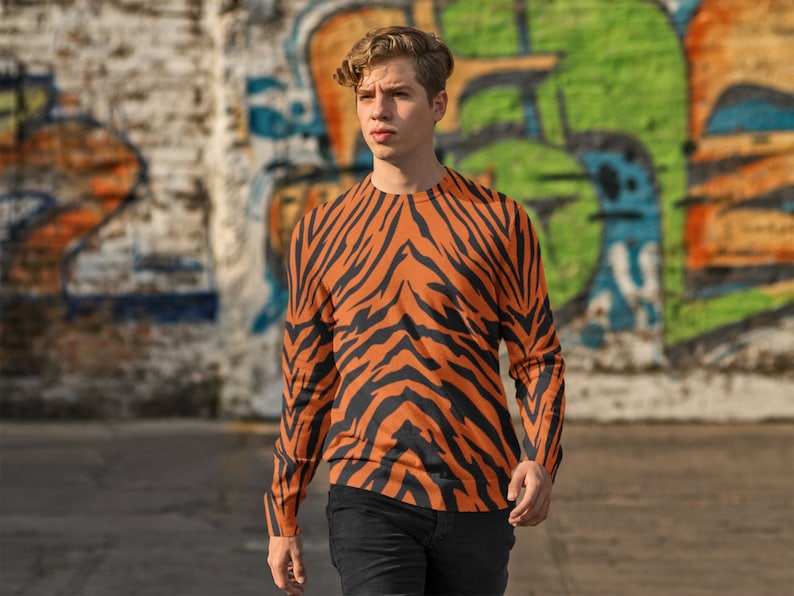 Op de afbeelding: Een shirt met lange mouwen met een oranje en zwart tijgerstreepdessin. Het shirt is gemaakt van een zacht, comfortabel materiaal en heeft een ontspannen pasvorm.