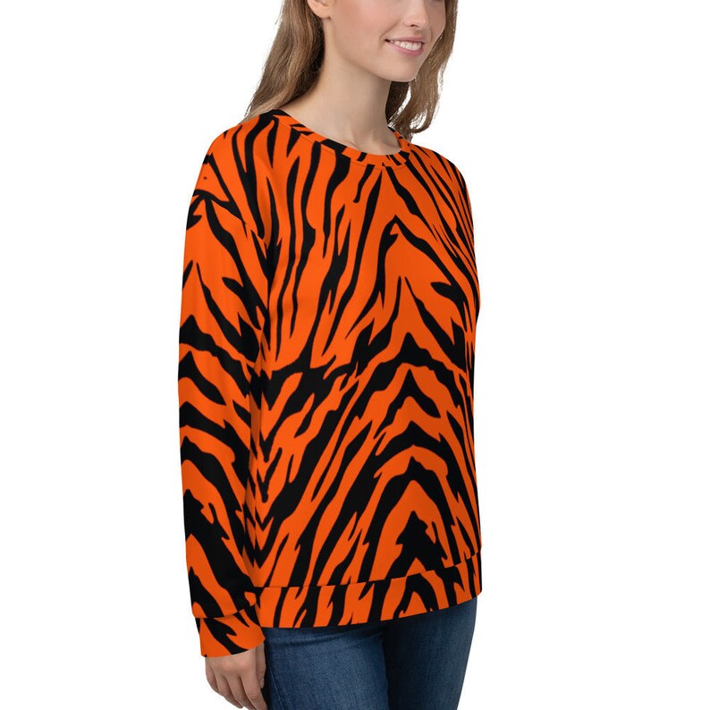 Op de afbeelding: Oranje en zwart gestreept sweatshirt met tijgerprint. Het sweatshirt heeft lange mouwen en een ronde hals.