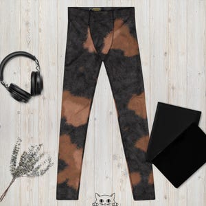 May include: Black and brown patterned leggings. The leggings have a dark grey base with irregular brown patches. A pair of black headphones, two black rectangles, and a sprig of dried flowers are also in the image.