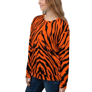 Op de afbeelding: Oranje en zwart gestreept sweatshirt met tijgerprint. Het sweatshirt heeft een ronde hals en lange mouwen.