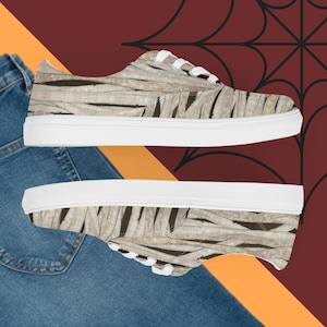 Könnte beinhalten: Leinenschuhe mit einem Mumien-Design. Die Schuhe haben ein beige-braunes Wickelmuster, weiße Schnürsenkel und eine weiße Gummisohle. Der Hintergrund ist im Halloween-Stil gehalten.
