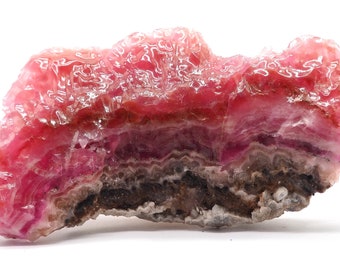 May include: A pink and brown banded mineral specimen with a layered, crystalline texture. The mineral has a smooth, polished surface and a slightly translucent appearance.