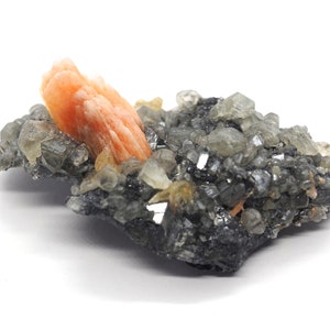 Puede incluir: Un grupo de cristales grises y transparentes con un gran cristal naranja en la parte superior. Los cristales están sobre una roca gris oscura.