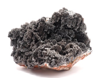 May include: A large, dark gray, crystalline rock formation with a rough, textured surface. The rock has a cluster of small, pointed crystals that resemble a cluster of tiny, black flowers.