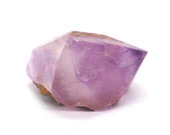 May include: A faceted amethyst crystal with a light purple hue. The crystal has a rough, natural base and a polished, pointed top. The stone is set against a white background, highlighting its color and form.