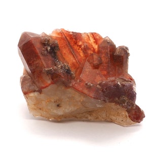 Peut inclure: Un groupe de cristaux de quartz rouge et transparent avec une texture brute et naturelle. Les cristaux sont regroupés dans une formation aléatoire, certains pointant vers le haut et d'autres vers le bas.