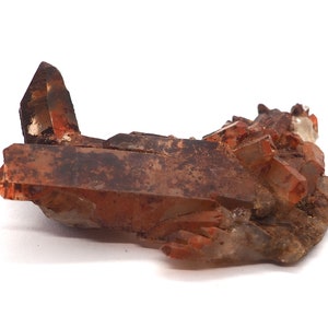 Peut inclure: Un amas de cristaux de quartz brun rougeâtre avec une texture naturelle rugueuse. Les cristaux sont regroupés en une formation aléatoire, certains pointant vers le haut et d'autres vers le bas. Les cristaux sont translucides et ont un léger éclat.