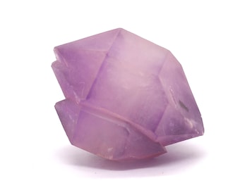 May include: A faceted, light purple crystal with a geometric shape. The crystal has a translucent quality, with visible internal structures and a subtle gradient of color. The crystal is set against a white background.