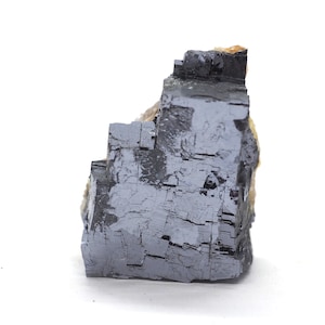 May include: A large, gray, cubic mineral specimen with a metallic sheen. The mineral has a rough, textured surface and appears to be composed of multiple smaller crystals.