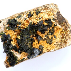 May include: A natural mineral specimen featuring a matrix of tan and beige rock. Dark, lustrous black crystals are clustered throughout, with areas of small, golden-yellow, granular formations. The overall appearance is rough and textured.