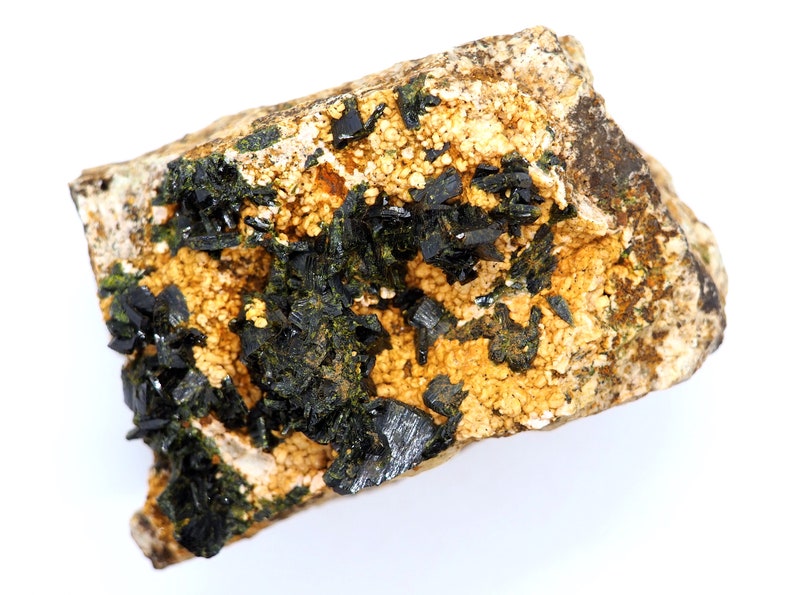 May include: A natural mineral specimen featuring a matrix of tan and beige rock. Dark, lustrous black crystals are clustered throughout, with areas of small, golden-yellow, granular formations. The overall appearance is rough and textured.