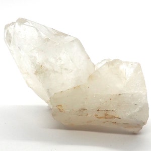 Peut inclure: Un amas de cristaux de quartz clair, avec un grand cristal pointu et un cristal plus petit attaché. Les cristaux sont translucides, avec des textures internes subtiles et une couleur blanc cassé clair. Le quartz est sur fond blanc.