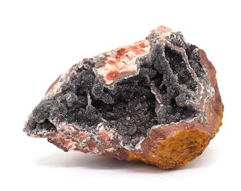 May include: A rough-hewn geode with a dark gray, crystalline interior. The exterior is a mix of reddish-brown and orange hues, with patches of white and red. The overall shape is irregular, showcasing natural formations.