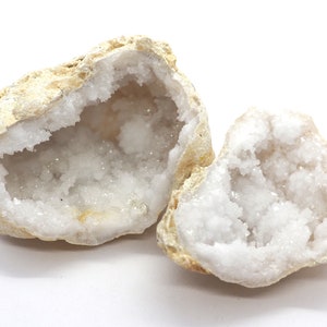 May include: Two halves of a white quartz geode with a rough exterior and a sparkling, crystalline interior.