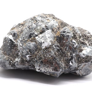 Può includere: Una roccia grigia ruvida con cristalli color argento incorporati. La roccia ha un aspetto naturale e non levigato.