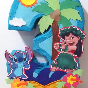 Puede incluir: Una pi&ntilde;ata azul con forma de n&uacute;mero tres con un sol azul, amarillo y naranja, una palmera verde con cocos marrones, una nube blanca, un personaje azul Stitch, un personaje rosa Lilo y flores de hibisco rosas y naranjas.