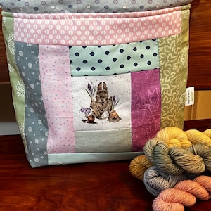 May include: A patchwork fabric drawstring bag with a bunny rabbit design and a label that says "Made with Love". The bag is filled with colorful yarn skeins in shades of yellow, green, blue, and pink.