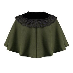 May include: An olive green capelet featuring a wide, rounded neckline adorned with a black lace trim. The garment has a flared, circular silhouette that drapes outward from the neck, with a visible vertical seam running down the center front.