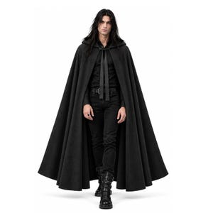 May include: A floor-length black hooded cloak featuring a wide, flowing silhouette and a simple tie closure at the neck. The garment is worn over a black button-down shirt, black trousers with a belt, and black leather boots with buckles.