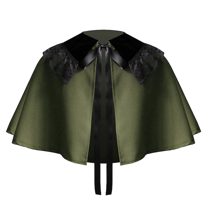 May include: An olive green capelet featuring a wide black velvet collar with black lace trim along the edges. The garment is secured at the neckline with a black satin ribbon tie that hangs down the front, creating a structured, flared silhouette.