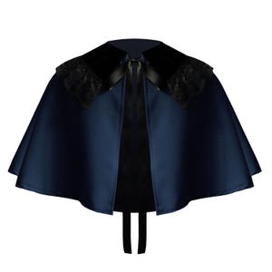 May include: A dark navy blue satin capelet featuring a wide black velvet collar with black lace trim on the shoulders. The garment is secured at the neckline with a black satin ribbon tie that hangs down the front, creating a structured silhouette.