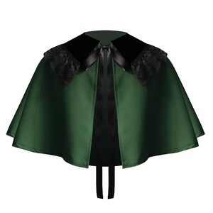 May include: A forest green capelet featuring a wide black velvet collar adorned with black lace trim along the edges. The garment is secured at the neckline with a black satin ribbon tie that hangs down the front, creating a structured silhouette.