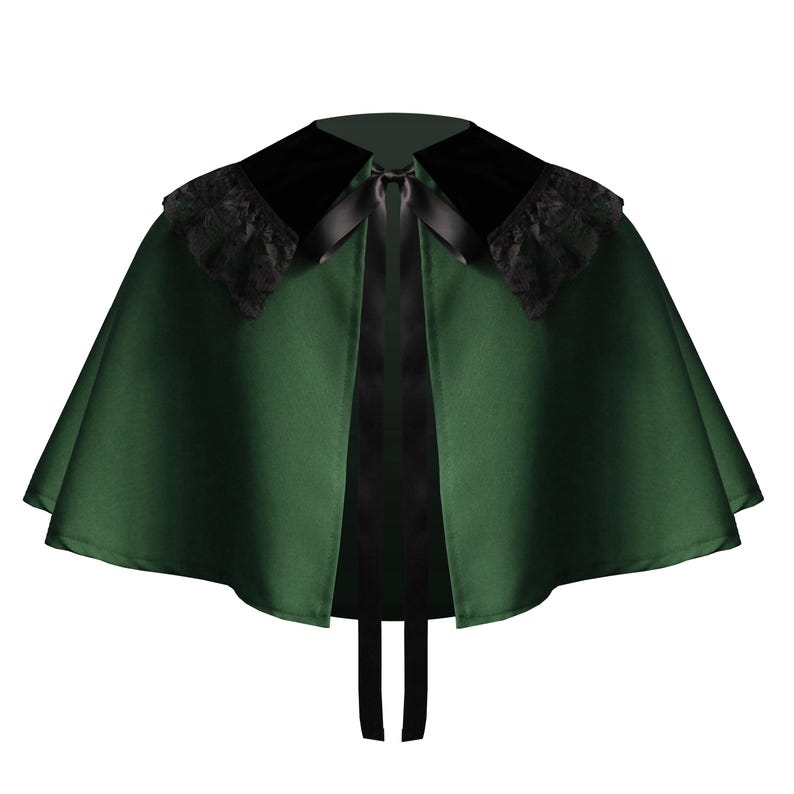 May include: A forest green capelet featuring a wide black velvet collar adorned with black lace trim along the edges. The garment is secured at the neckline with a black satin ribbon tie that hangs down the front, creating a structured silhouette.