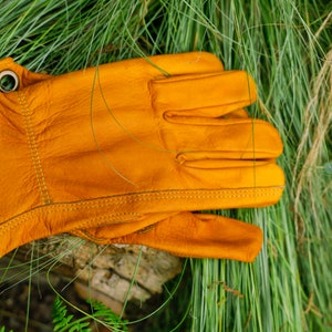 May include: A pair of yellow leather work gloves with a stitched seam detail. The gloves have two metal eyelets on the wrist.