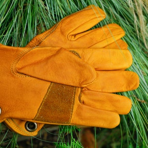May include: A pair of brown leather work gloves with a suede patch on the back of the hand. The gloves have a reinforced thumb and index finger.