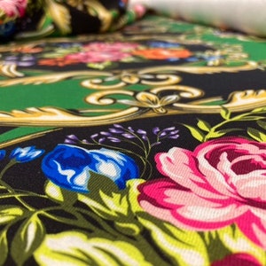 Könnte beinhalten: Grüner, schwarzer und weißer Stoff mit einem Blumenmuster. Der Stoff zeigt große rosa Rosen, blaue Blumen und goldene Akzente.
