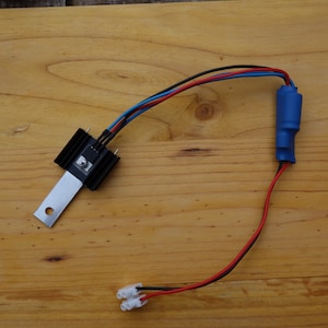 Peut inclure: Un composant électronique noir avec un dissipateur thermique et une plaque métallique argentée, relié à des fils rouges, noirs et bleus. Les fils sont reliés à un tube thermorétractable bleu et un connecteur blanc.