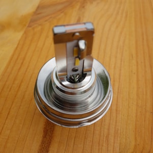 May include: Close-up of a silver and gold LED light bulb. The bulb has a metallic base and a rectangular light-emitting component. The light-emitting component has a small, yellow light source. The background is a wooden surface.