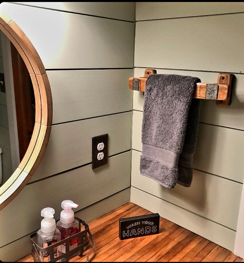 May include: A bathroom scene featuring a wooden towel rack with a gray towel. The rack is mounted on a light green wall. A round mirror and a soap dispenser are also visible. A sign that says "WASH YOUR HANDS" is on the counter.