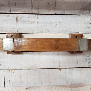 May include: A rustic wooden shelf made from reclaimed barrel wood. The shelf is a warm brown color with metal brackets on each end. The shelf is mounted on a white and light brown wooden wall.