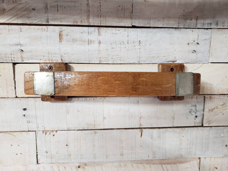 May include: A rustic wooden shelf made from reclaimed barrel wood. The shelf is a warm brown color with metal brackets on each end. The shelf is mounted on a white and light brown wooden wall.