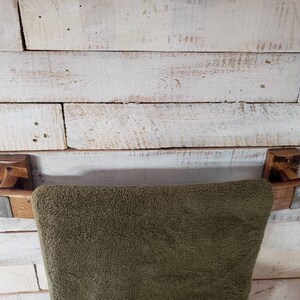 May include: A rustic wooden towel rack with a dark brown finish, mounted on a white-painted wooden wall. The rack features a dark green towel. The rack's design incorporates metal accents.