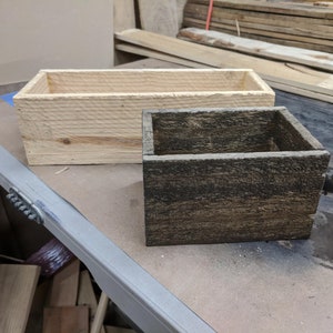 May include: Two wooden boxes, one is natural wood and the other is stained dark brown. Both boxes are rectangular and have a rustic look.