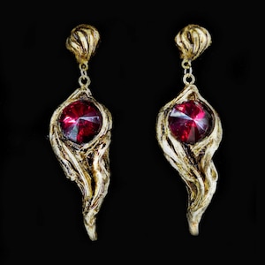 May include: A pair of gold-tone earrings with a red gemstone set in a twisted, organic-shaped design.