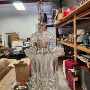 May include: A vintage clear glass pendant light fixture with a decorative, textured design. The light hangs from a silver-colored chain and canopy. The glass shade has a tulip shape with a scalloped edge.