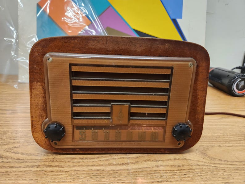 Puede incluir: Radio de madera vintage con marco rectangular y panel frontal marr&oacute;n claro. La radio presenta listones horizontales y un dial con n&uacute;meros. Dos perillas negras a cada lado. Una pieza cl&aacute;sica de decoraci&oacute;n del hogar.