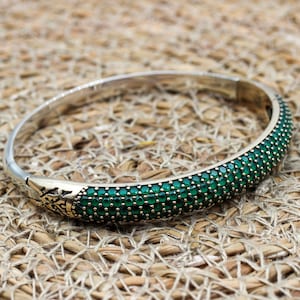 Peut inclure: Un bracelet jonc en argent avec un motif décoratif et une rangée de pierres précieuses vertes.