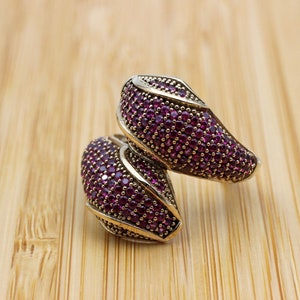 May include: A silver ring with a unique design featuring two curved, overlapping sections, each encrusted with small, purple gemstones.