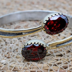 May include: A silver and gold bangle bracelet with two large red oval-shaped gemstones.