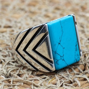 May include: A silver ring with a turquoise stone set in a geometric design.