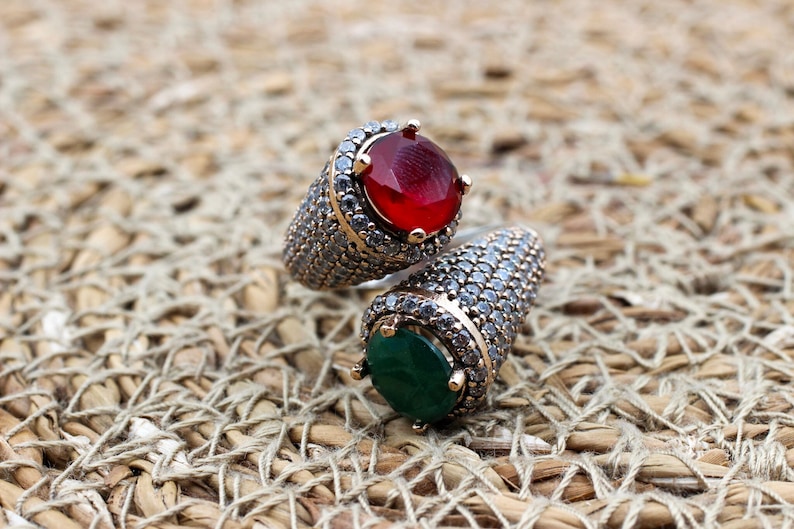May include: Two silver rings with a red and green gemstone. The rings are set with small clear stones.