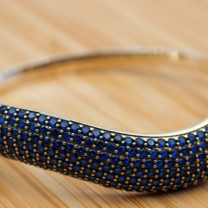May include: A silver bangle bracelet with a wave-like design, encrusted with small, dark blue gemstones.