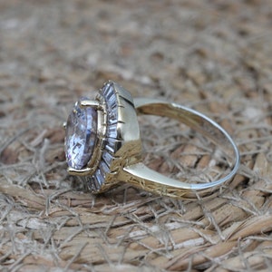 K&ouml;nnte beinhalten: Ein goldener Ring mit einem gro&szlig;en, klaren, ovalen Edelstein, der von einem Heiligenschein aus kleineren, klaren Edelsteinen umgeben ist.