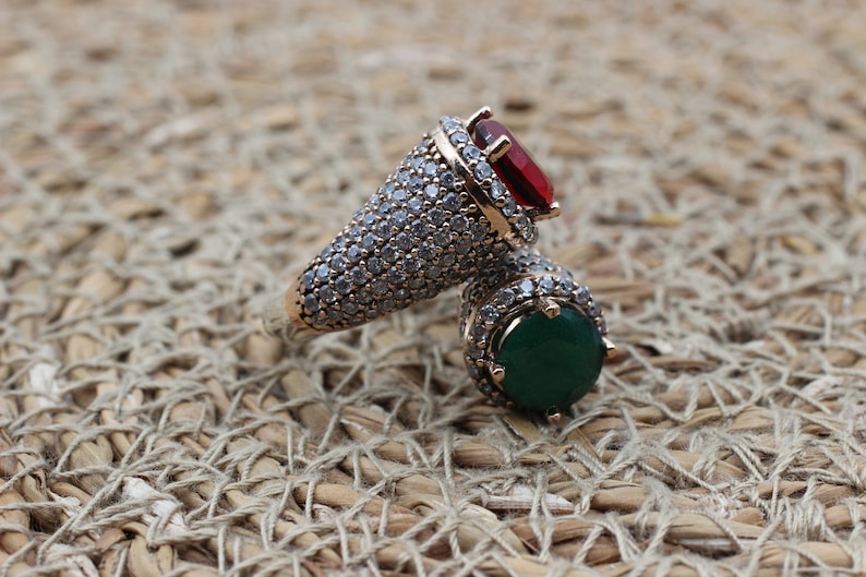 May include: A gold ring with a red and green gemstone setting. The ring is covered in small, clear stones.
